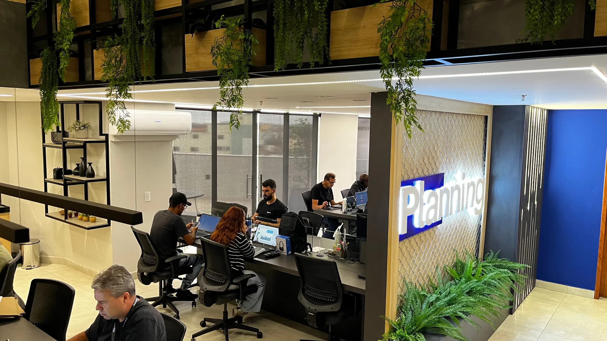 Equipe Planning trabalhando no escritório, com letreiro da marca ao fundo